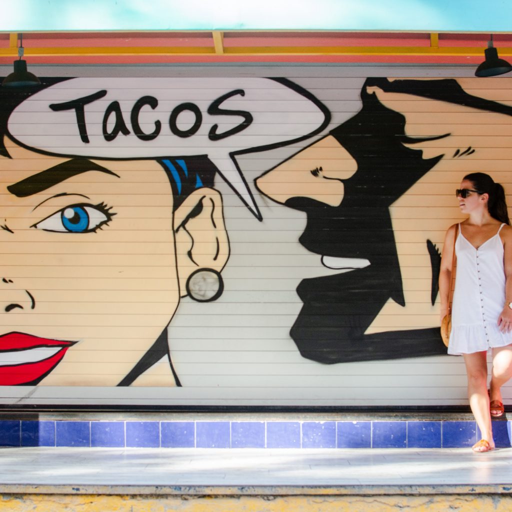 solo female traveler poses with street art painted on a taco shop sign in Playa del Carmen Mexico