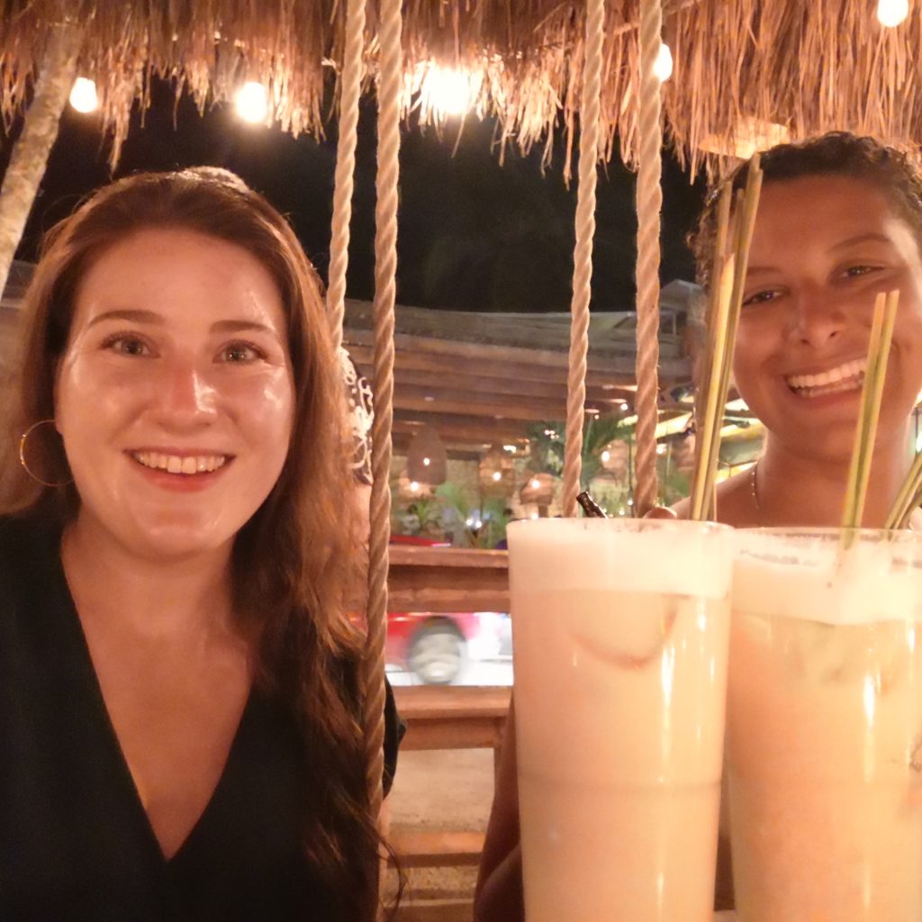 Two solo female travelers drinking pina coladas at a bar in Mexico to demonstrate solo female travel safety tips like going out with drinking buddies