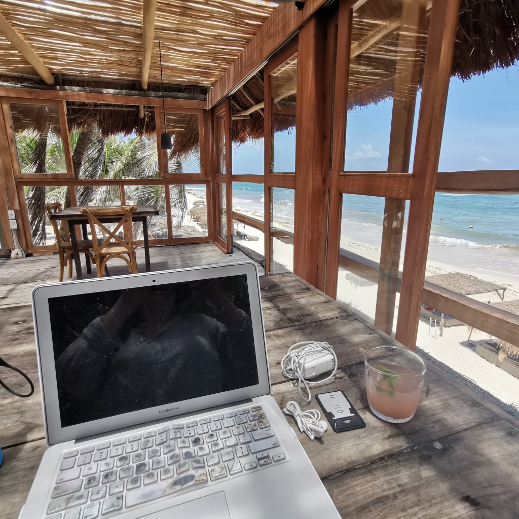 Digital nomad works with her laptop and a cocktail at a beach bar in Tulum, Mexico