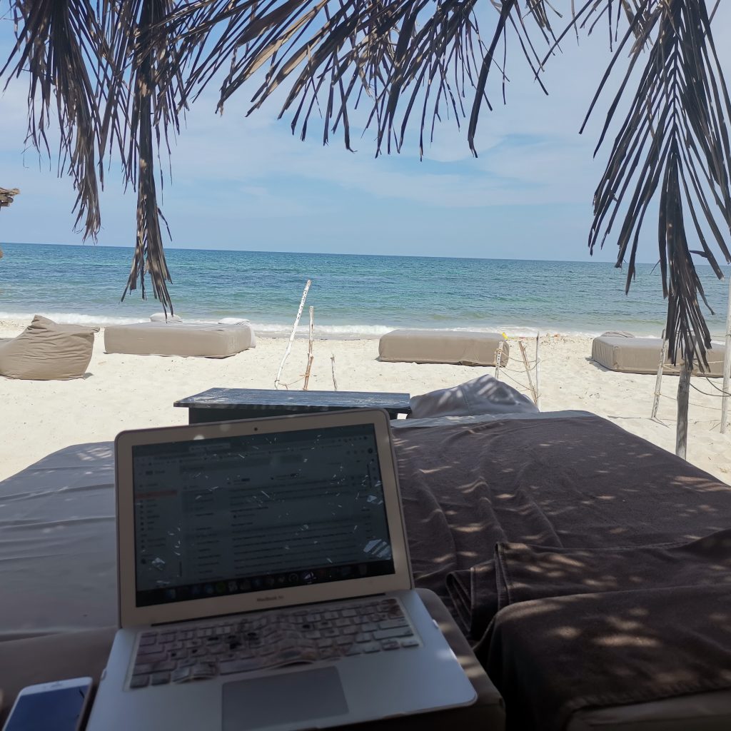 Digital nomad works with her laptop on a beach lounger on the beach in Tulum, Mexico