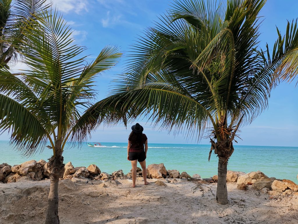 Solo female traveler between palm trees on the beach in Isla Holbox Mexico on a budget vacation